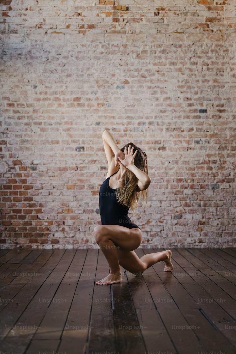 a woman kneeling on a wooden floor in front of a brick wall