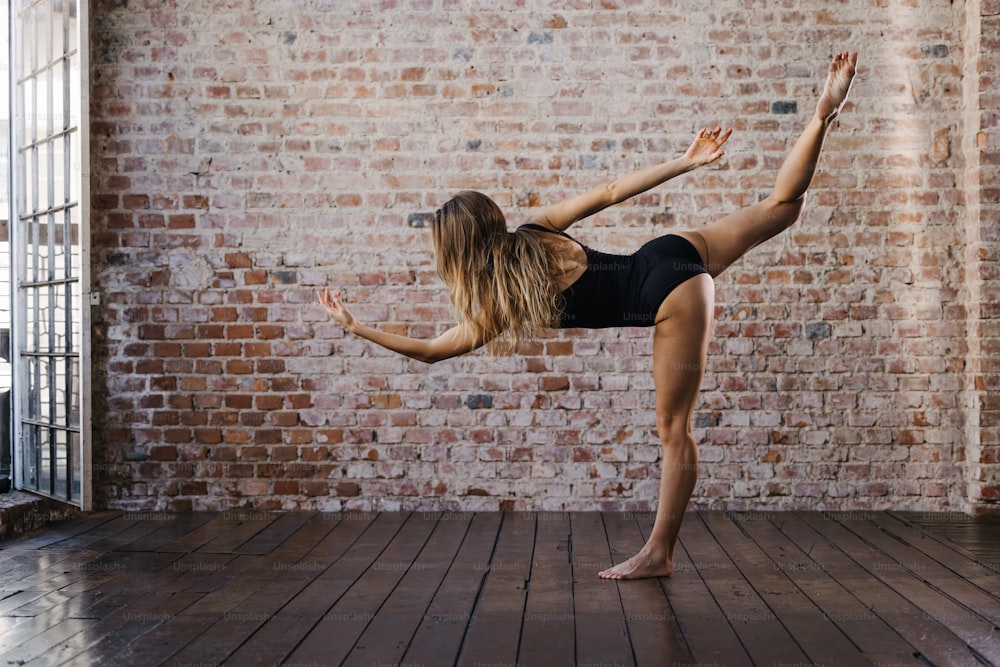 Una mujer haciendo una pose de yoga frente a una pared de ladrillos