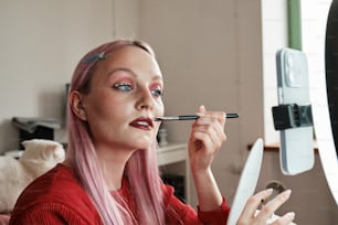 a woman with pink hair is doing makeup