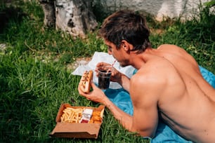 Un hombre sin camisa comiendo un perrito caliente y papas fritas