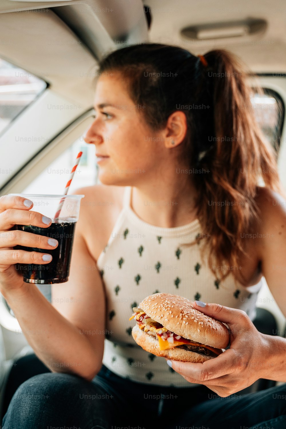 uma mulher sentada em um carro segurando um sanduíche e uma bebida