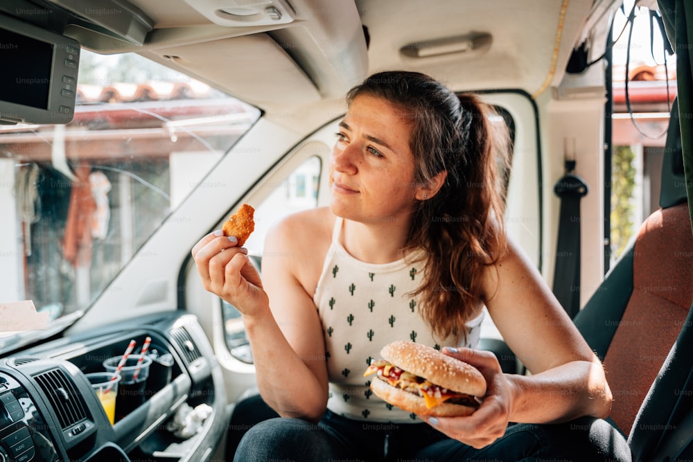 uma mulher sentada em um carro comendo um sanduíche