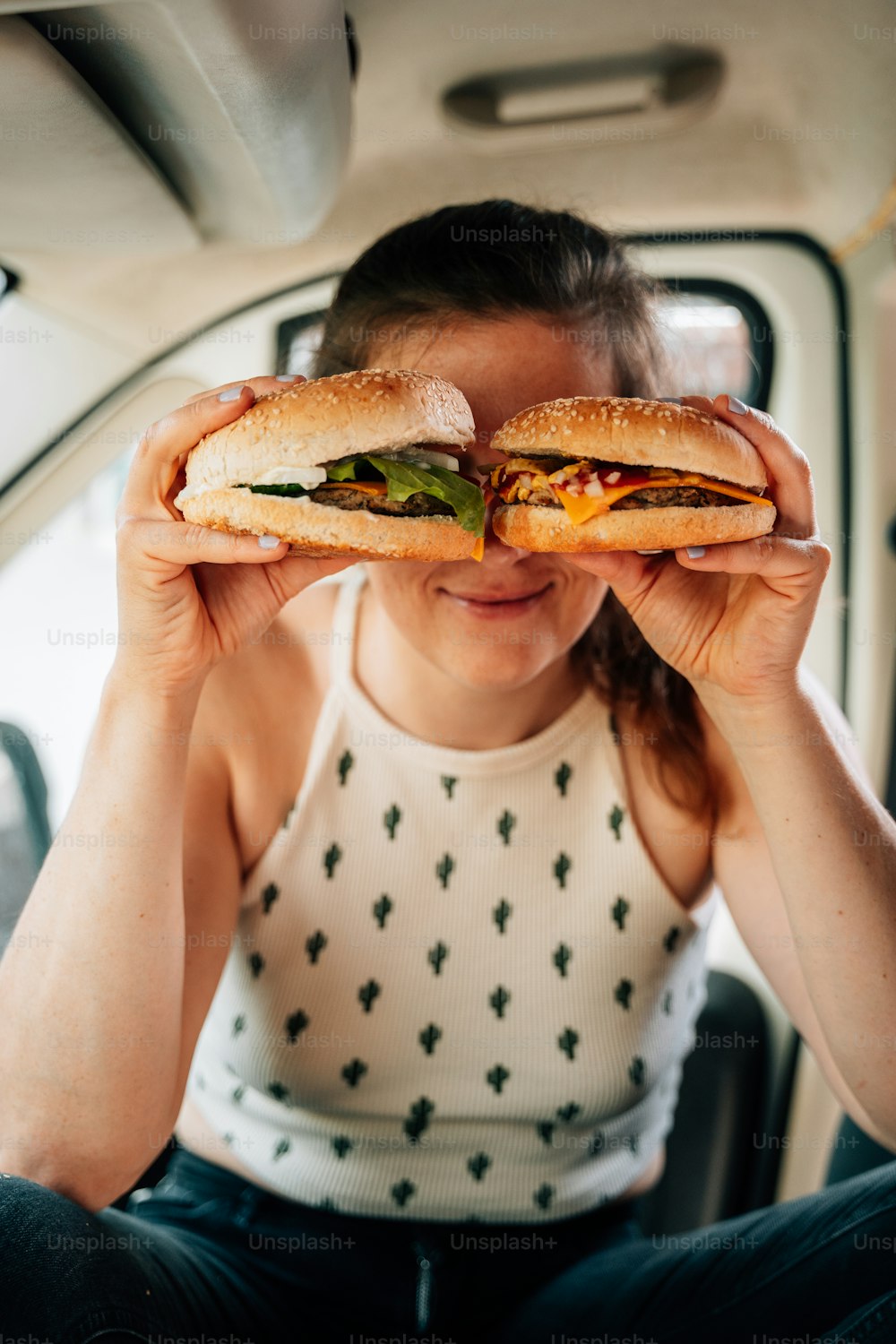 Una mujer sentada en la parte trasera de un automóvil sosteniendo un sándwich frente a ella