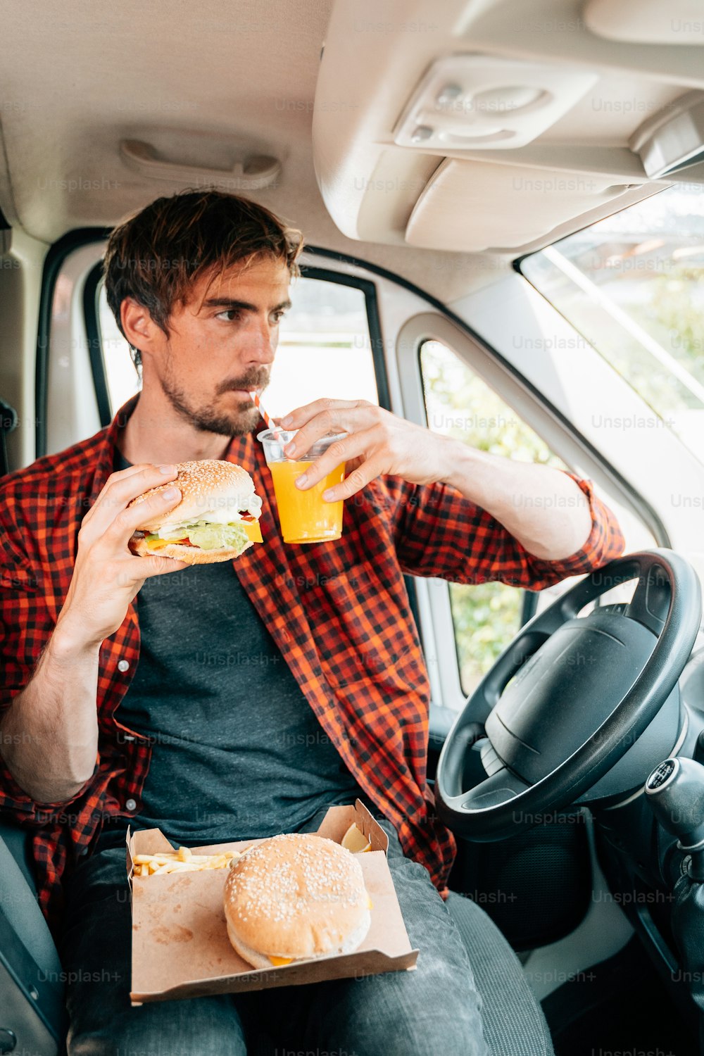 a man sitting in the back seat of a car eating a sandwich and drinking a