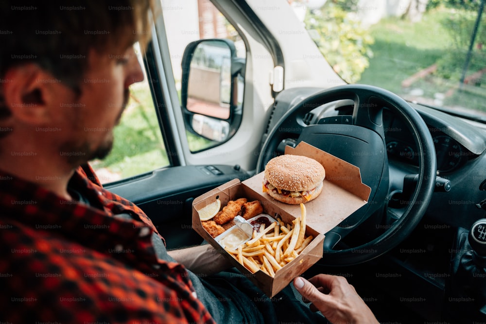 Un uomo seduto in una macchina con in mano una scatola di cibo