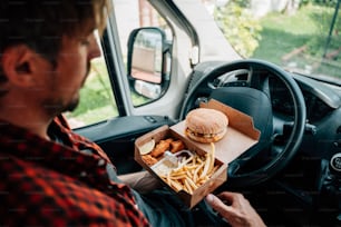 um homem sentado em um carro segurando uma caixa de comida
