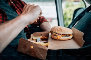 um homem sentado em um carro comendo um hambúrguer e batatas fritas