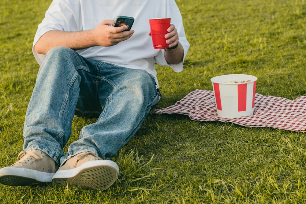 um homem sentado na grama segurando um copo vermelho