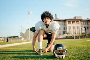 um homem ajoelhado em um campo de futebol ao lado de um capacete