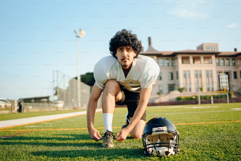 a man kneeling on a football field next to a helmet