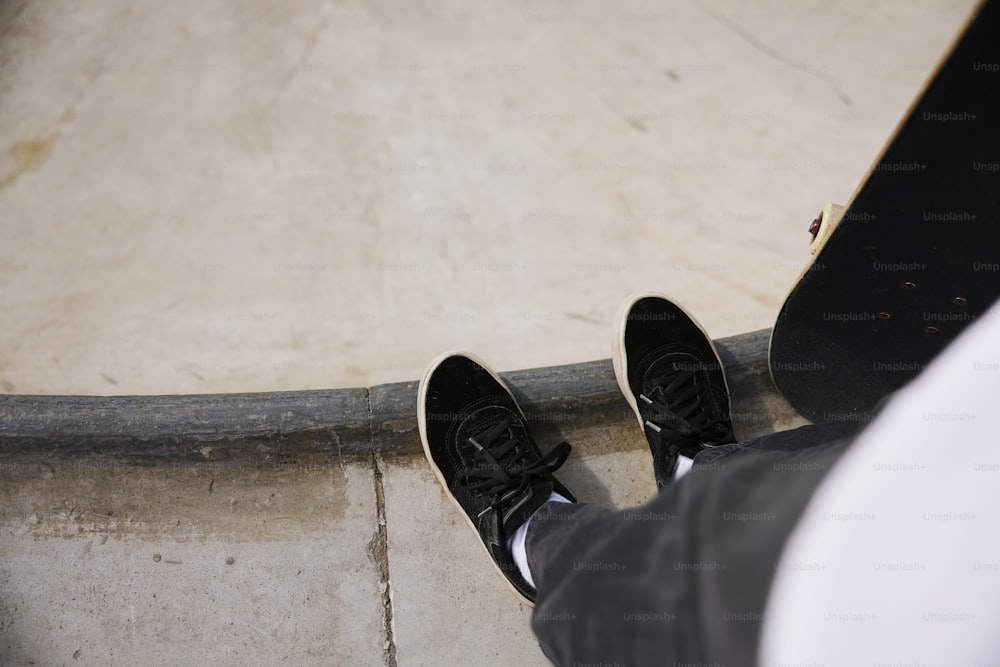 a person wearing black shoes standing next to a skateboard