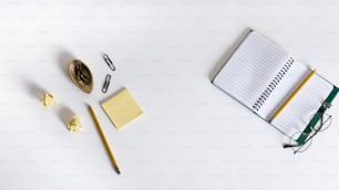 a desk with a notebook, pen, eyeglasses, and other items