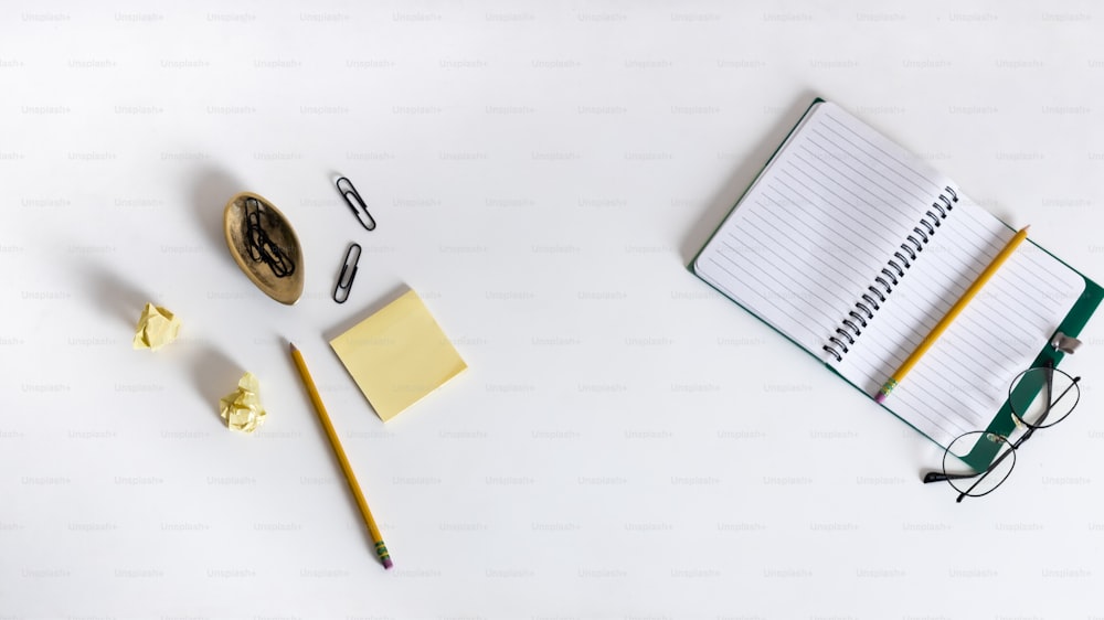 a desk with a notebook, pen, eyeglasses, and other items