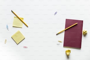 un cuaderno, lápiz y otros suministros de oficina sobre una superficie blanca