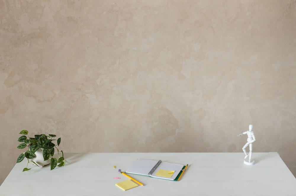 Una mesa blanca con una planta y un cuaderno