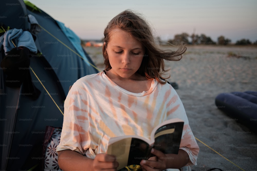 uma menina lendo um livro na praia