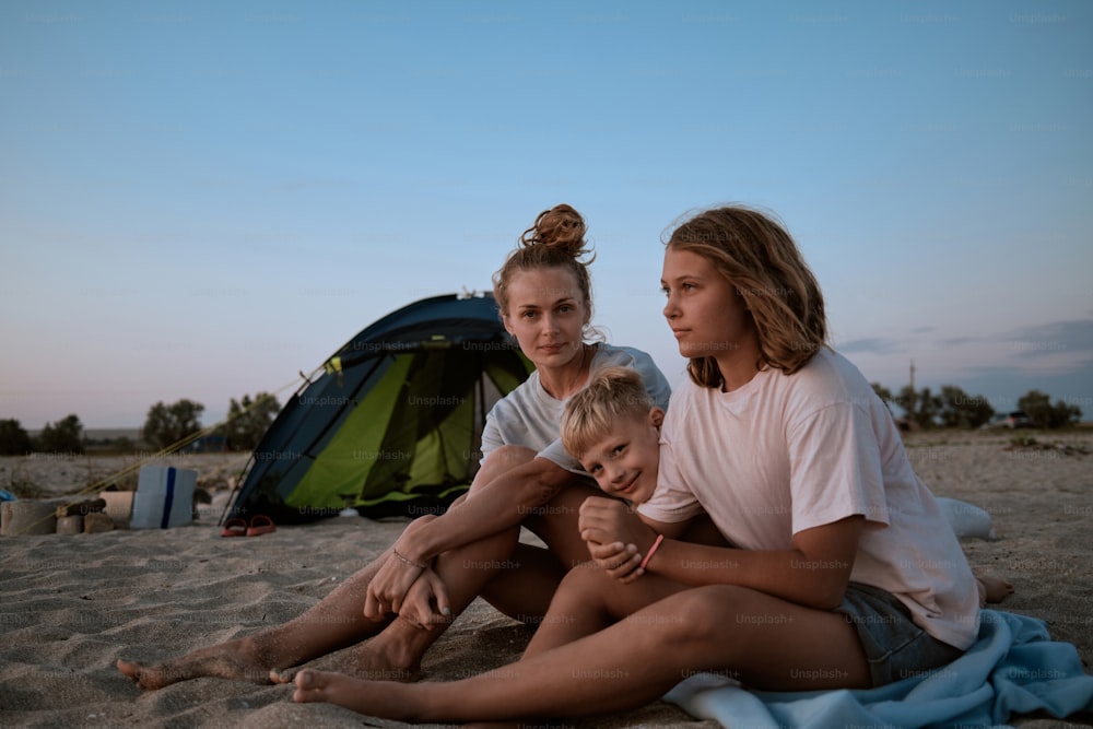 텐트 옆 해변에 앉아 있는 여자와 아이