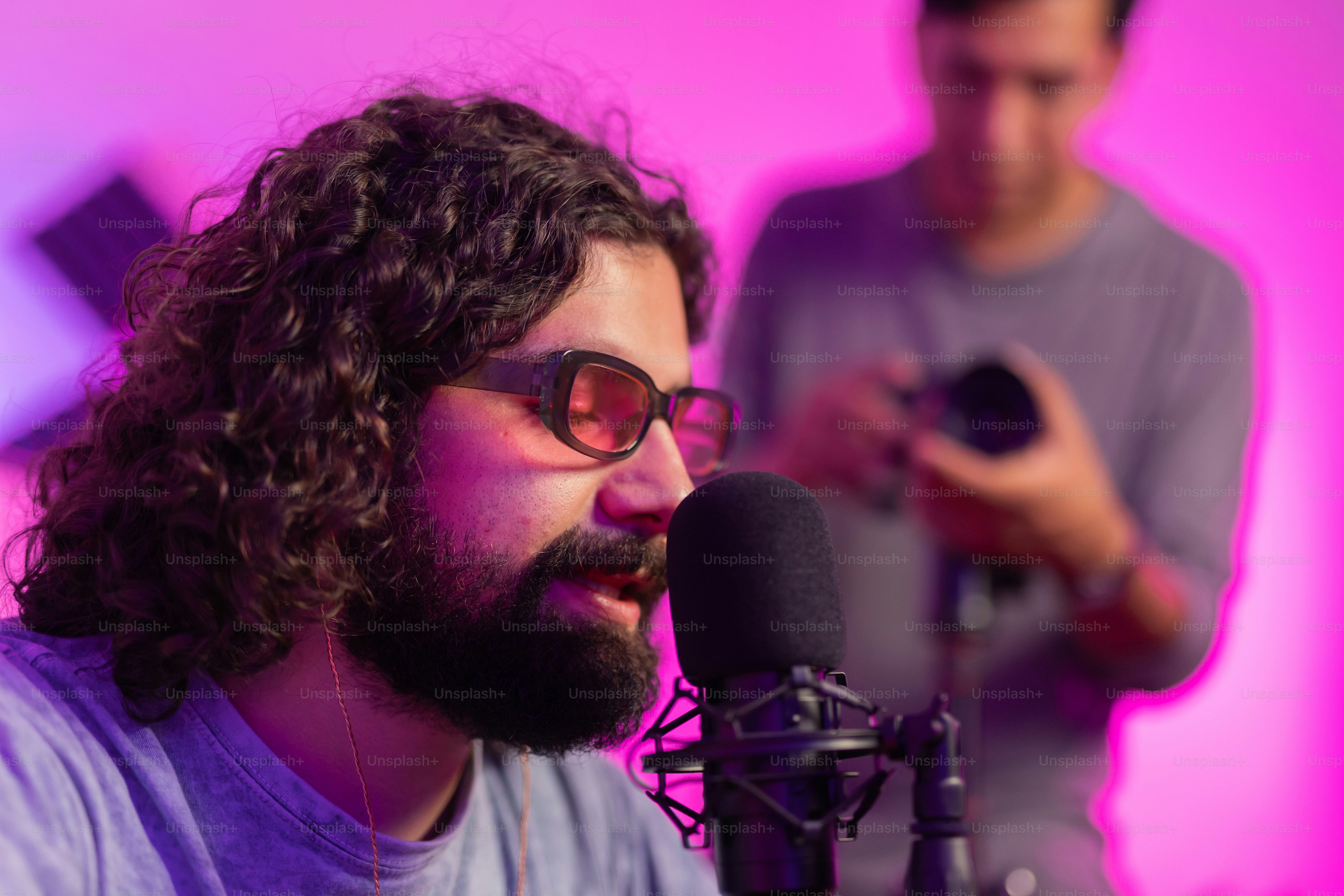 a man with long curly hair and glasses is singing into a microphone