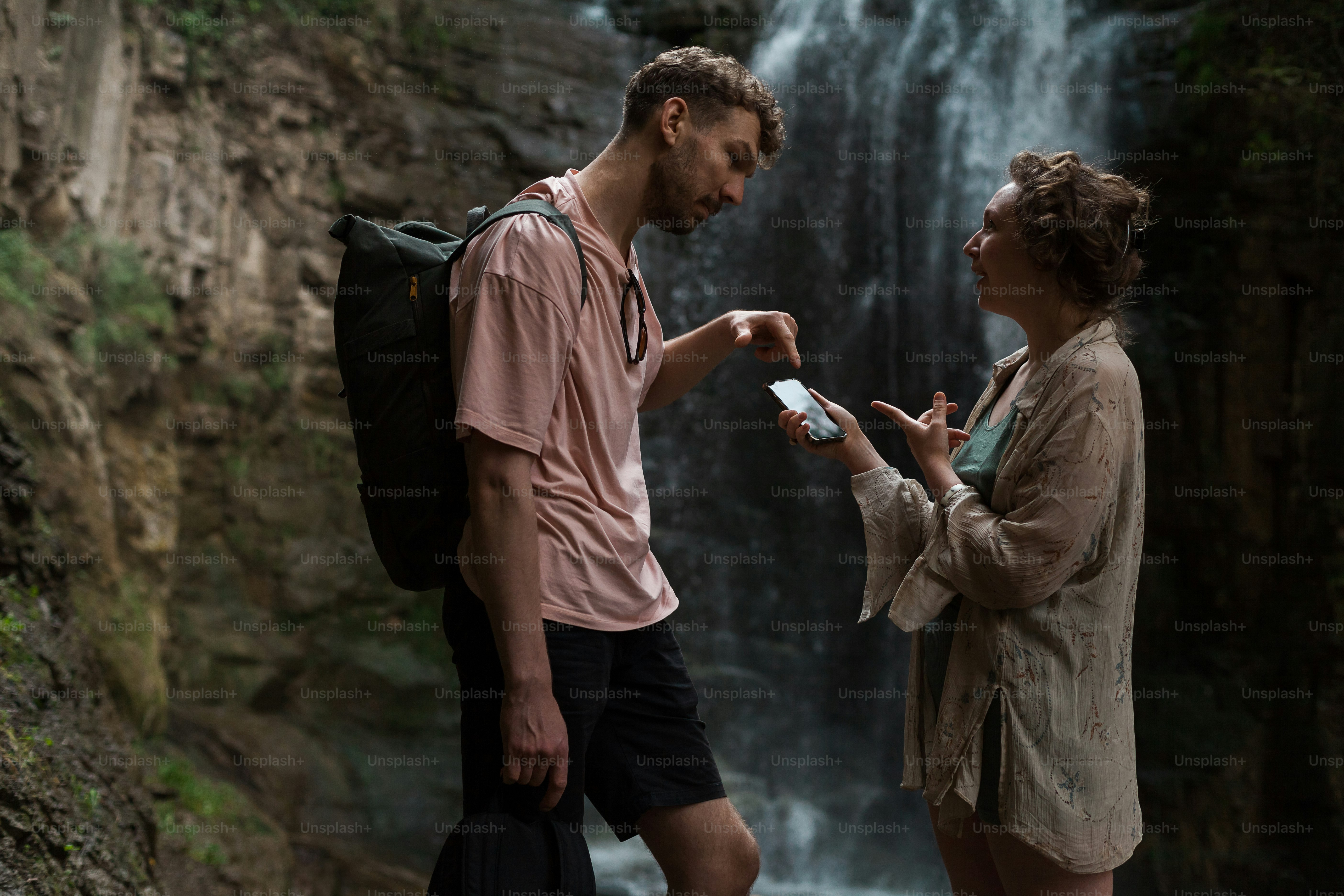 a man and a woman standing in front of a waterfall