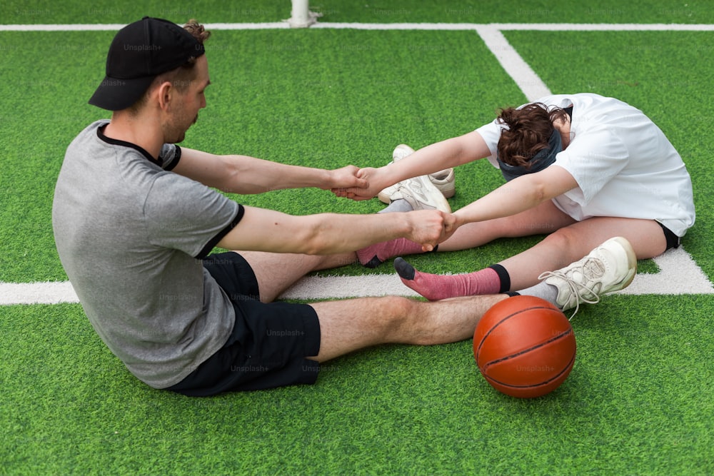 a man and a woman sitting on the ground with a basketball