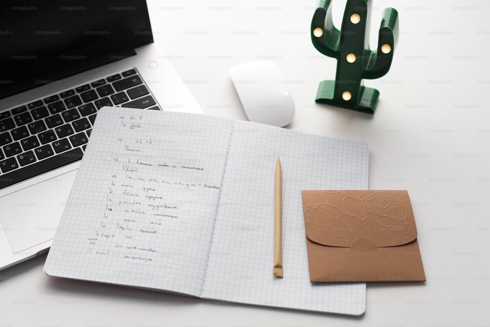 ein aufgeschlagenes Notizbuch, das auf einem Schreibtisch neben einem Laptop sitzt