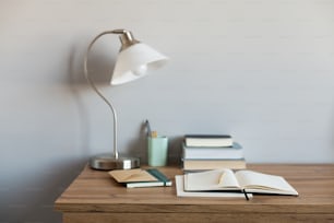 a desk with a lamp, books and a pen on it