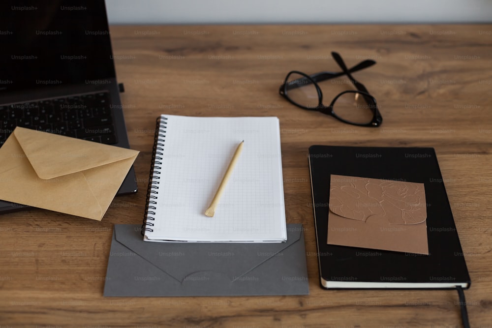 una scrivania con un taccuino, una penna, degli occhiali e un computer portatile