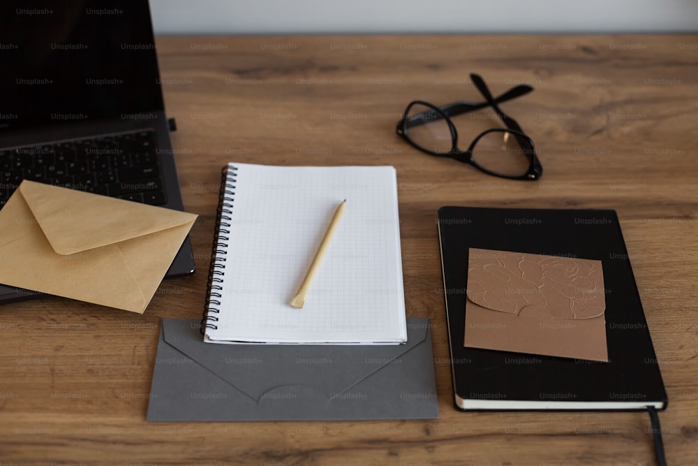 a desk with a notebook, pen, glasses, and a laptop on it