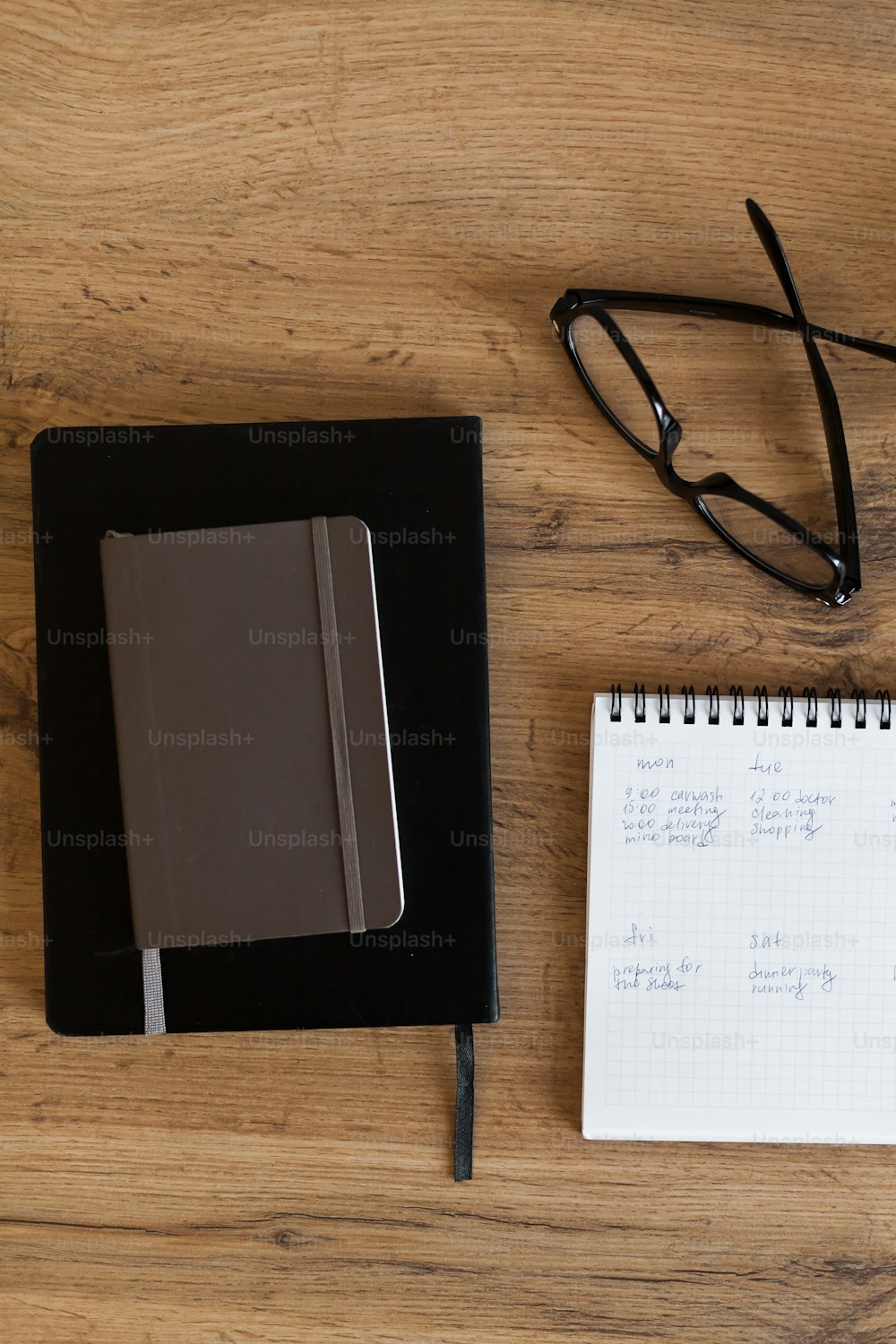 um bloco de notas, caneta, óculos e caderno sobre uma mesa de madeira