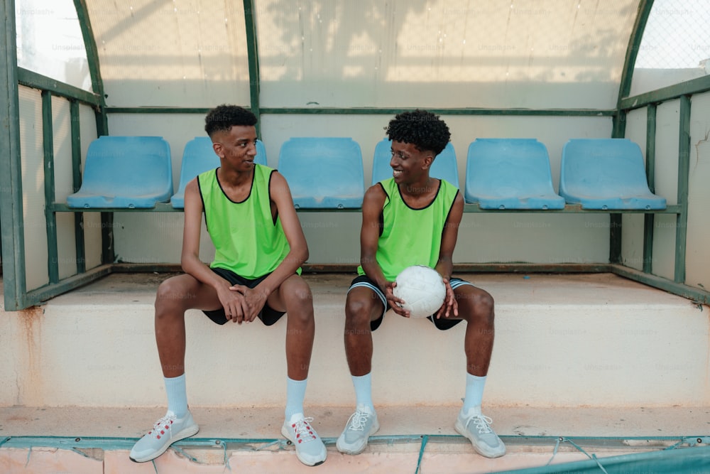two young men sitting on a bench with a ball