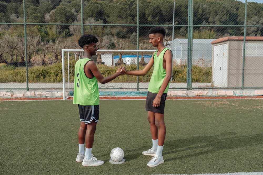 two young men shaking hands over a soccer ball