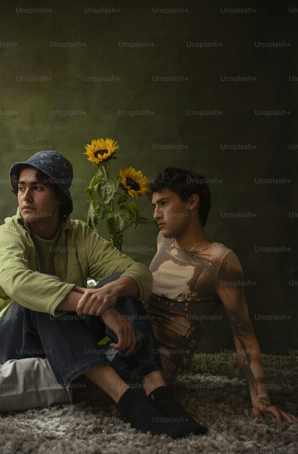 a man sitting on the ground next to a man with sunflowers