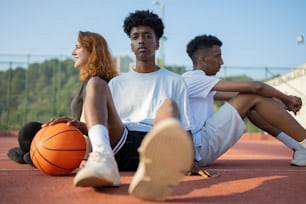 three people sitting on a court with a basketball