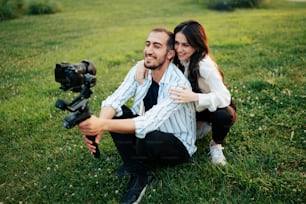 a man and woman sitting in the grass with a camera