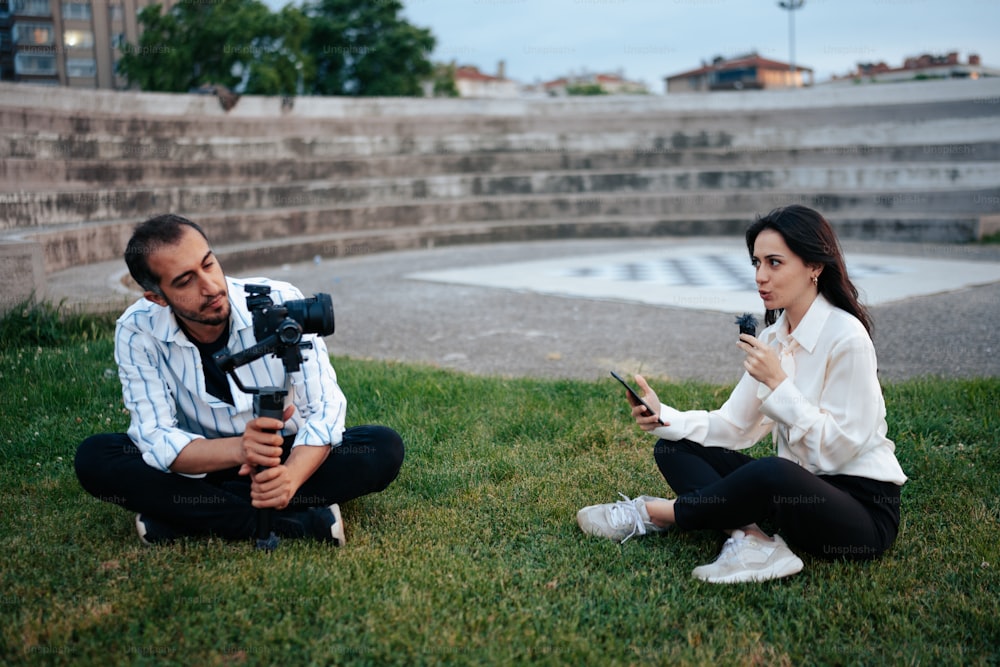 a man and a woman sitting on the grass with a camera