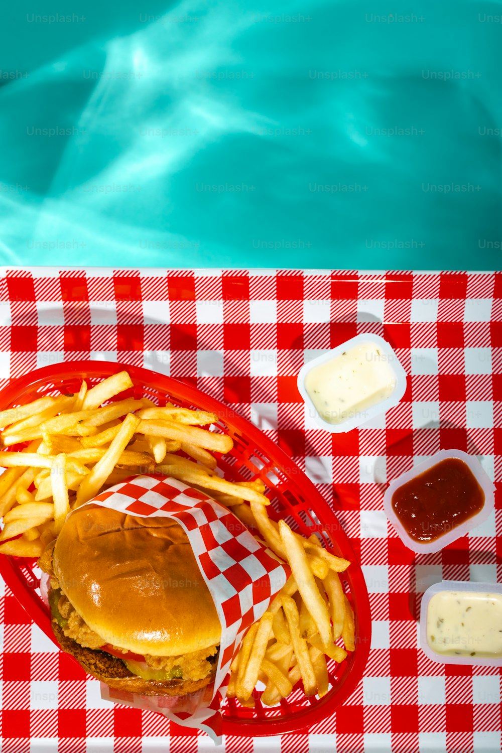 um hambúrguer e batatas fritas em uma toalha de mesa quadriculada vermelha e branca