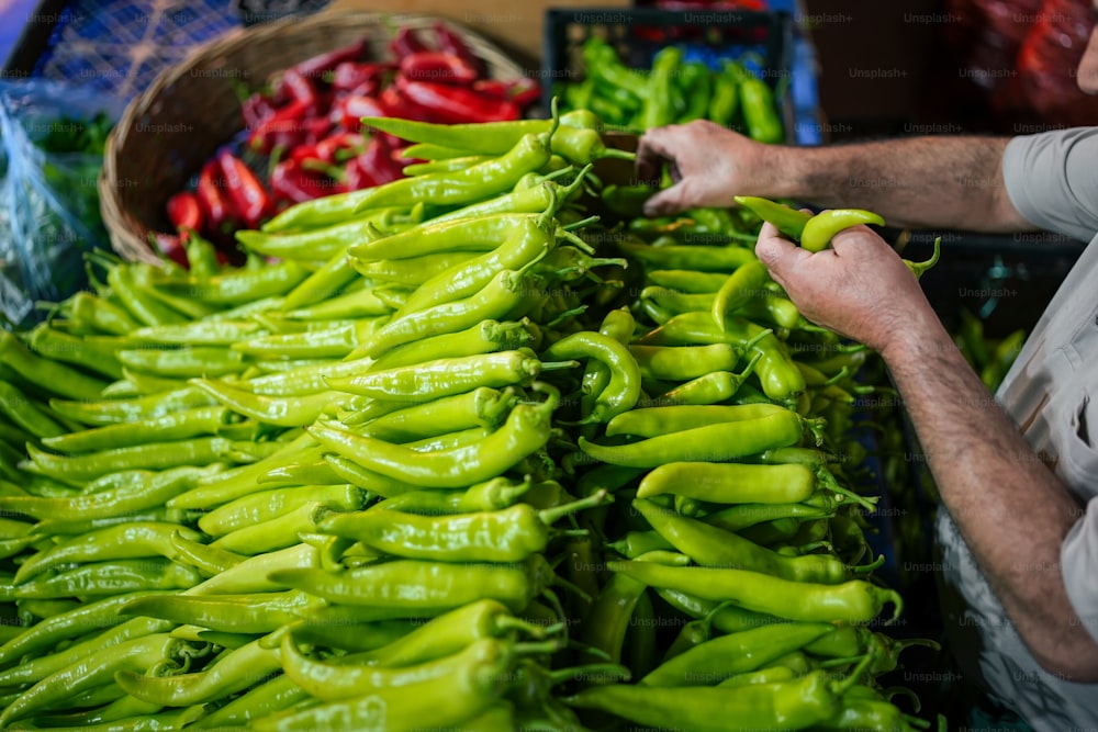 a man is picking up green peppers at a market