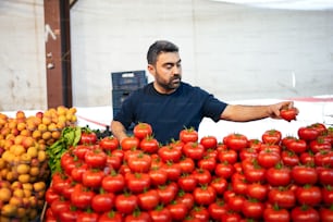 Un uomo in piedi davanti a un mucchio di pomodori