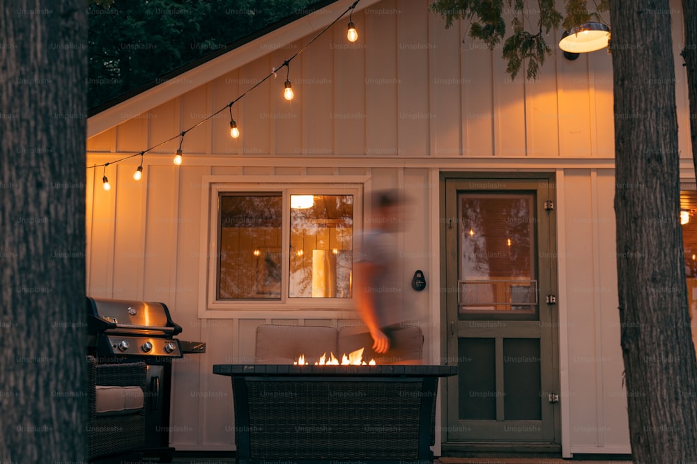 a man walking into a house with a fire pit in front of it