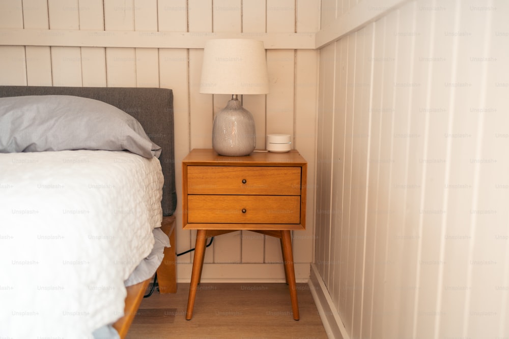 a nightstand with a lamp on top of it next to a bed