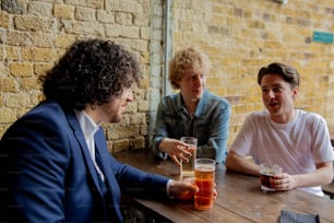 Tres hombres sentados en una mesa con bebidas frente a ellos
