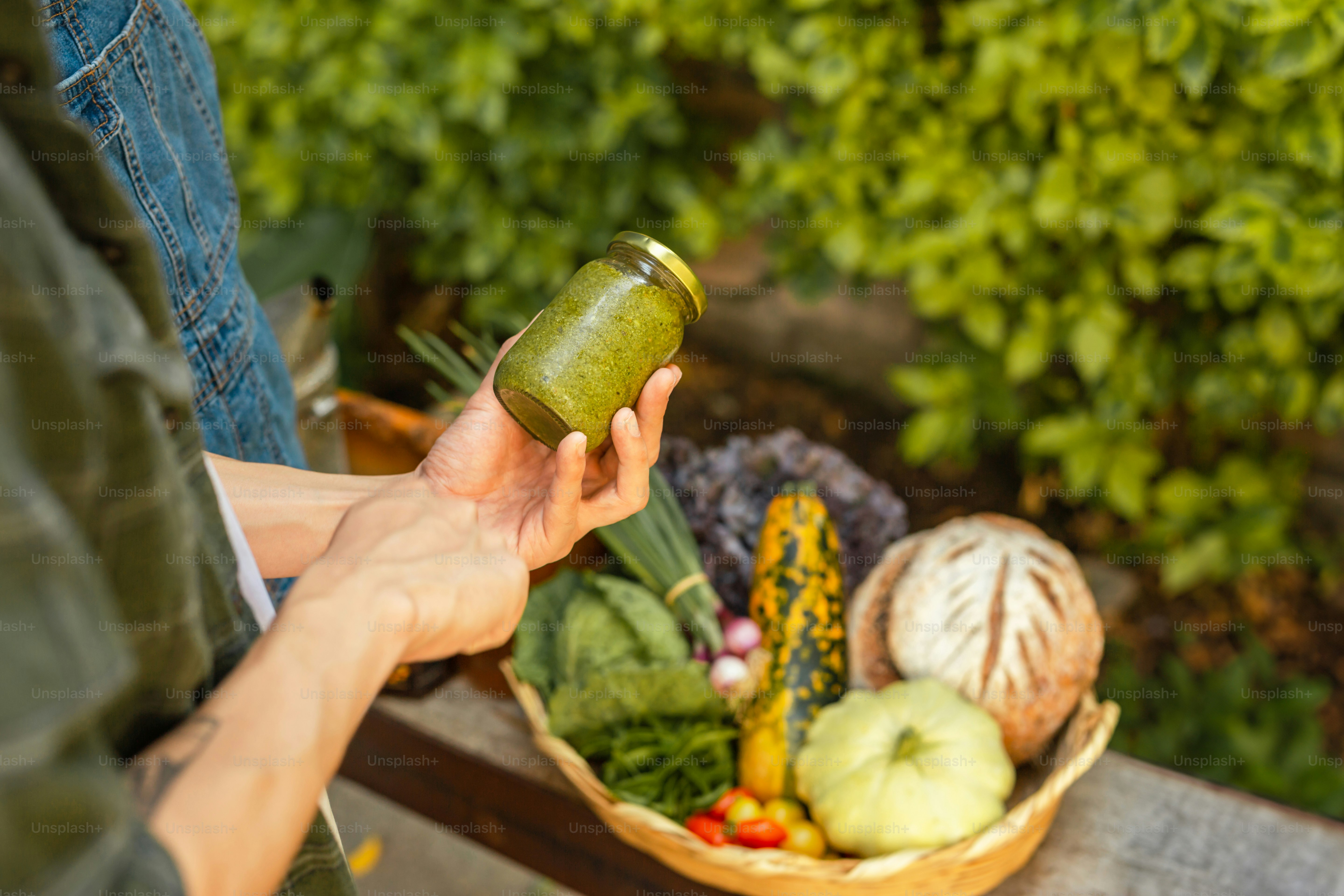 una persona che tiene un barattolo di sottaceti davanti a un cesto di verdure