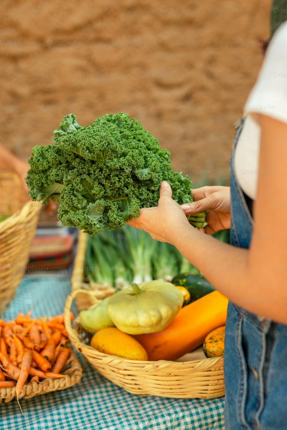 a woman holding a bunch of broccoli over a basket of carrots