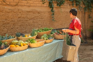 um menino em pé em frente a uma mesa cheia de cestos de legumes