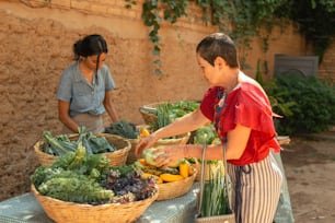 Un niño y una mujer de pie en una mesa con cestas de verduras