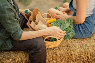 a man and a woman sitting on hay with a basket of vegetables