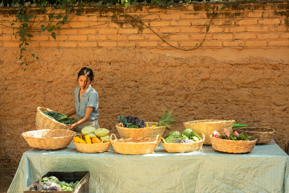 a woman standing in front of a table filled with baskets of vegetables