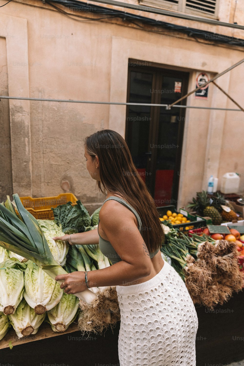 Una mujer parada frente a un puesto de frutas y verduras
