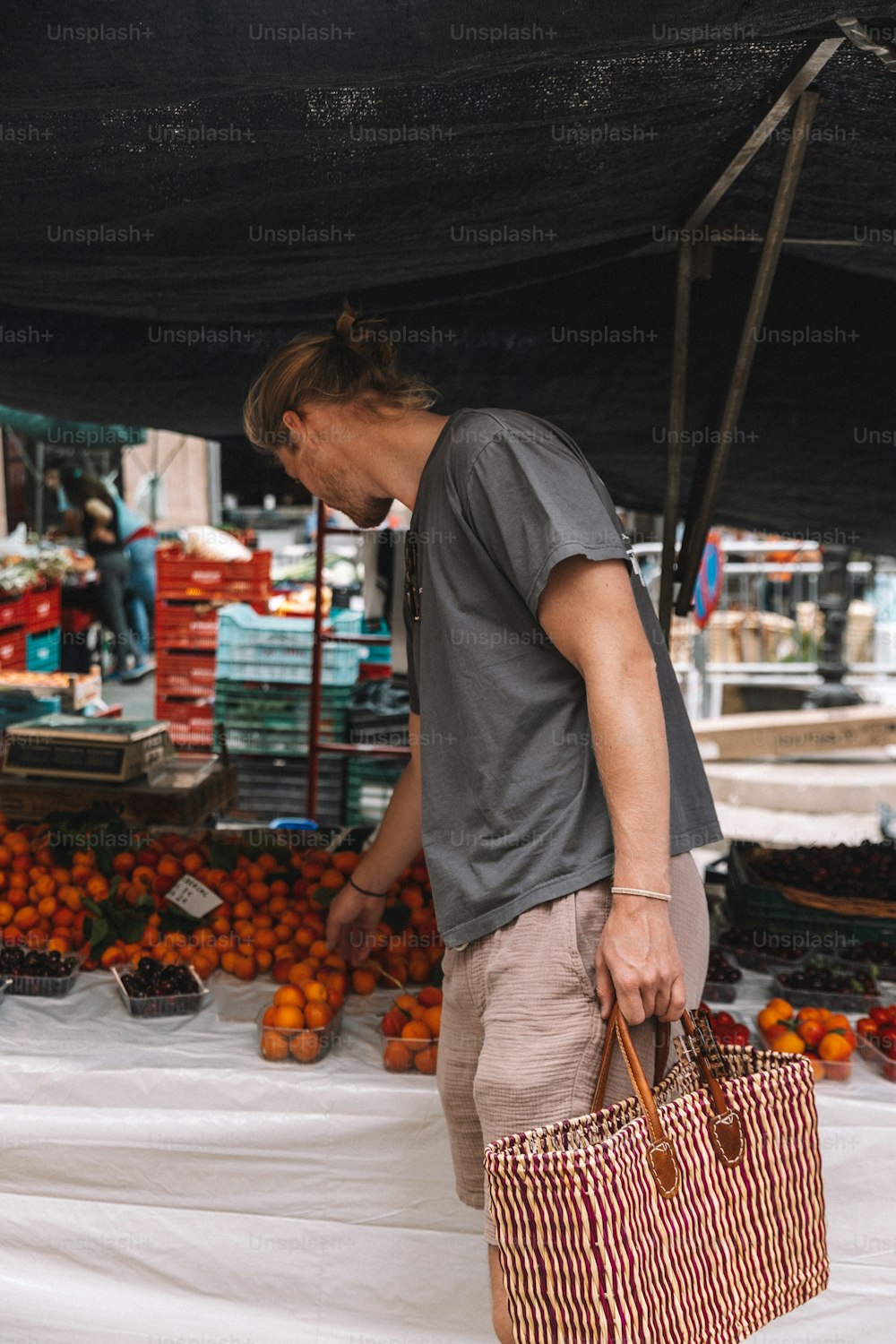 a man carrying a shopping bag in front of a fruit stand