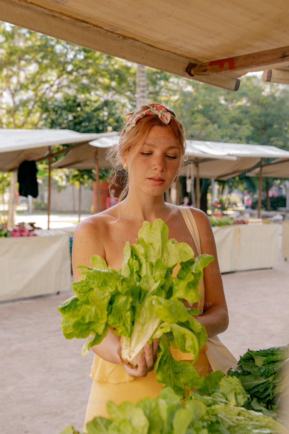 a woman in a yellow dress holding a bunch of lettuce